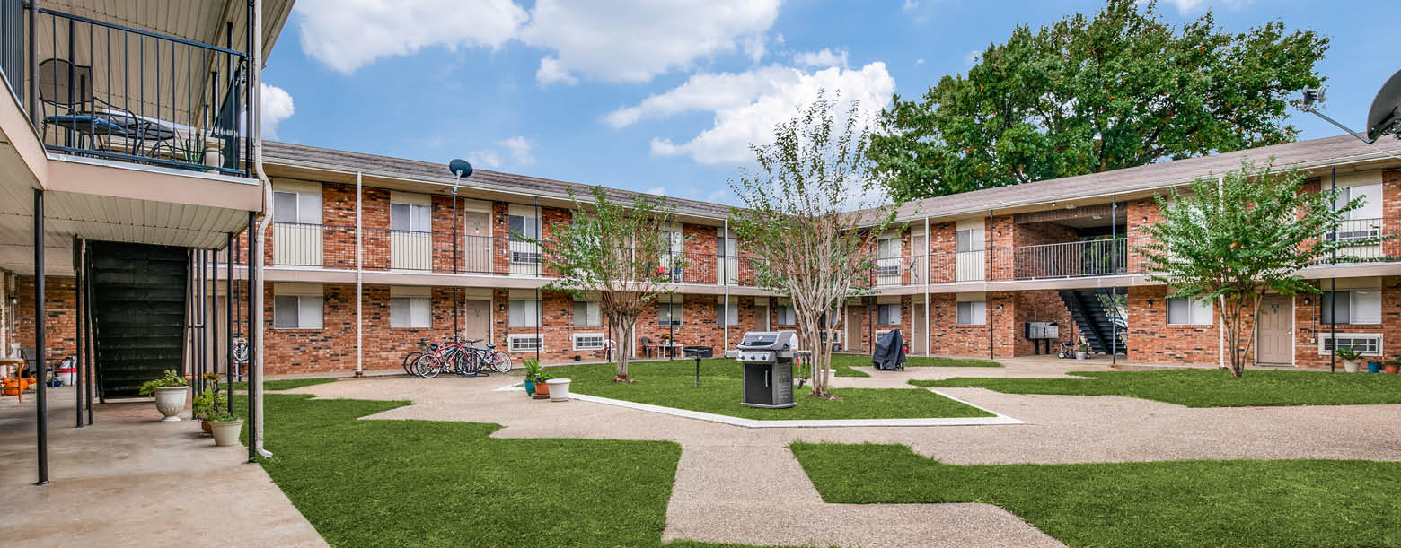 The courtyard at Hidden Oaks is equipped with grills and designed with landscaping. There are two-story buildings surrounding the square.
