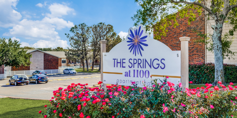 A view of the signage at The Springs at 1100, along with several buildings and a parking lot in the back.