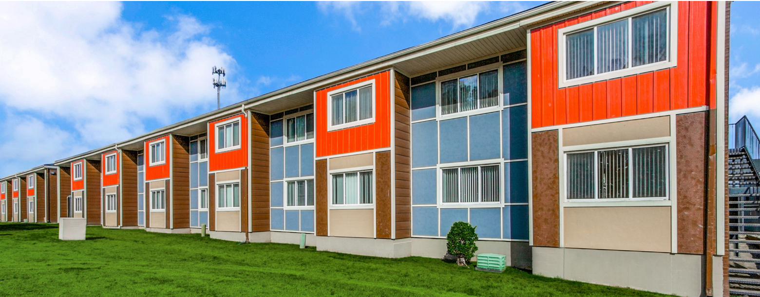 Colorful two-story multifamily housing with red and brown panels, large windows, and an external staircase on a grassy lawn.