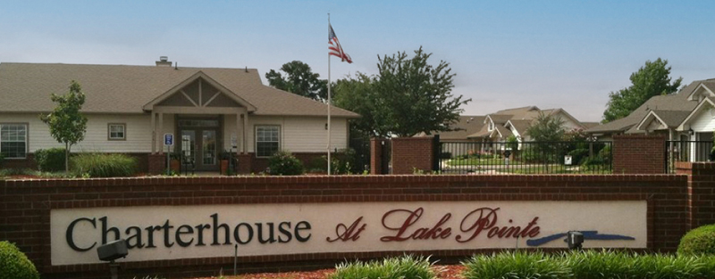 Brick sign reading 'Charterhouse at Lake Pointe' in front of a residential complex with American flag, under a cloudy sky.