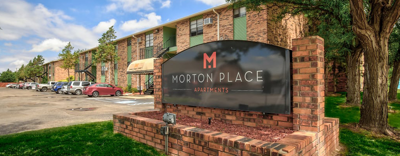 Morton Place Apartments brick sign in front of a two-story apartment building with parked cars and green trees.