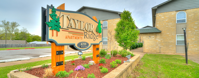 Colorful sign for Taylor Ridge Apartments with landscaping in front of a two-story brick building.