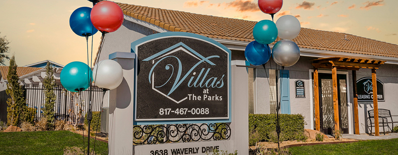 "Signage for 'Villas at The Parks' with balloons, in front of the community leasing center, under a partly cloudy sky at dusk.