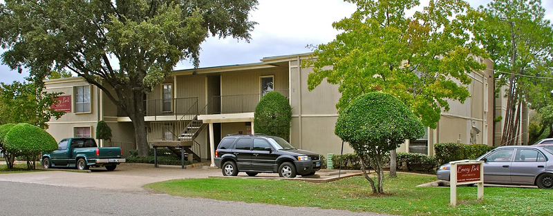 Exterior view of Dwellings at Kessler Park with two-story buildings, well-manicured trees, and parked cars.