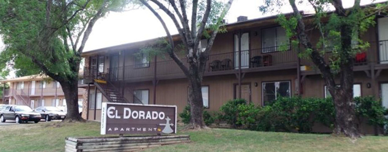 Exterior view of El Dorado Apartment building with two stories, trees in front, and a sign reading 'El Dorado Apartments' on the lawn.