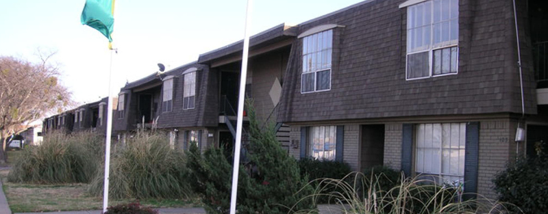 Exterior view of Pineview Apartments with two-story buildings, large windows, and surrounding greenery, featuring flagpoles in the foreground.
