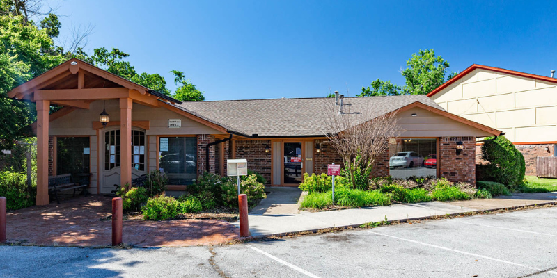 Leasing office of Foxcroft Apartments with a covered entryway, landscaped front, and a parking lot, on a bright sunny day.