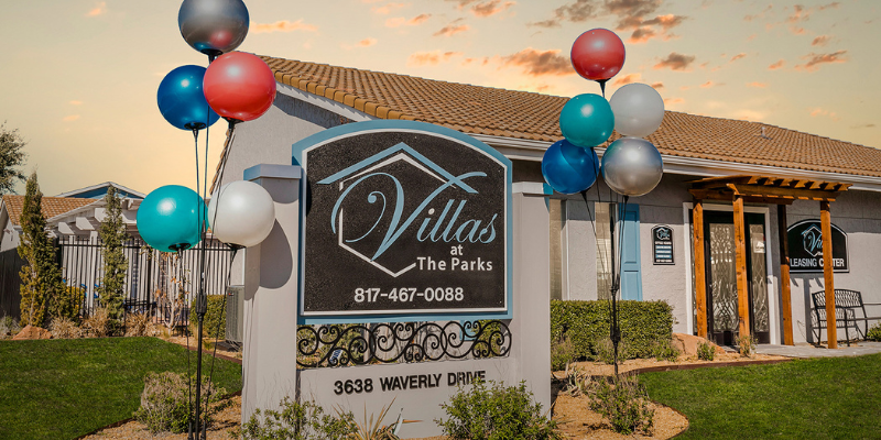 "Signage for 'Villas at The Parks' with balloons, in front of the community leasing center, under a partly cloudy sky at dusk.