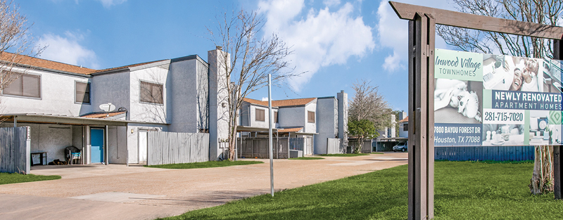 Two-story townhomes with gray exteriors, fenced patios, and a sign reading 'Inwood Village Townhomes, Newly Renovated Apartment Homes' in Houston, TX.