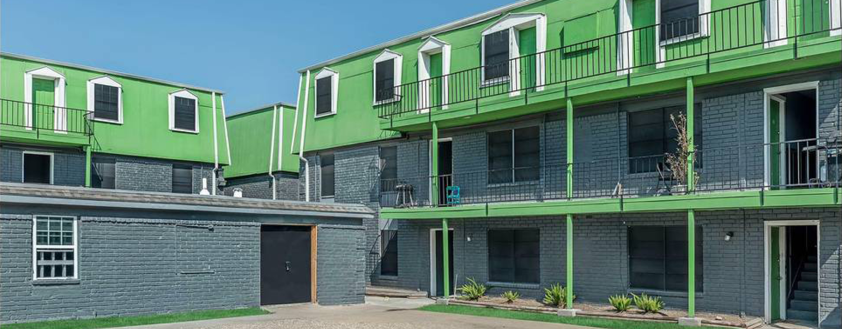 Three-story apartment complex with bold lime green upper facade, charcoal gray brick walls, and black railings; doors and trim are accented in bright green and white.