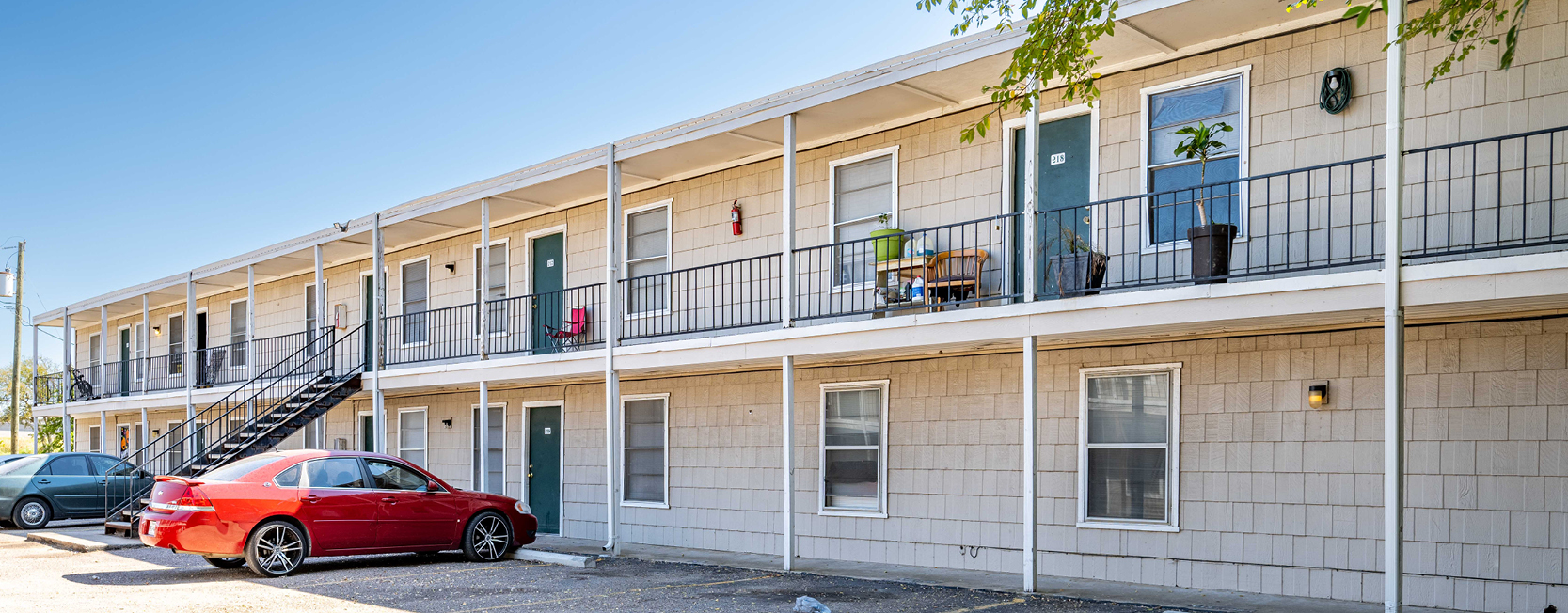 Two-story beige apartment building at Northwind Apartments in Waco, TX, with green doors, black railings, and parked cars in front.