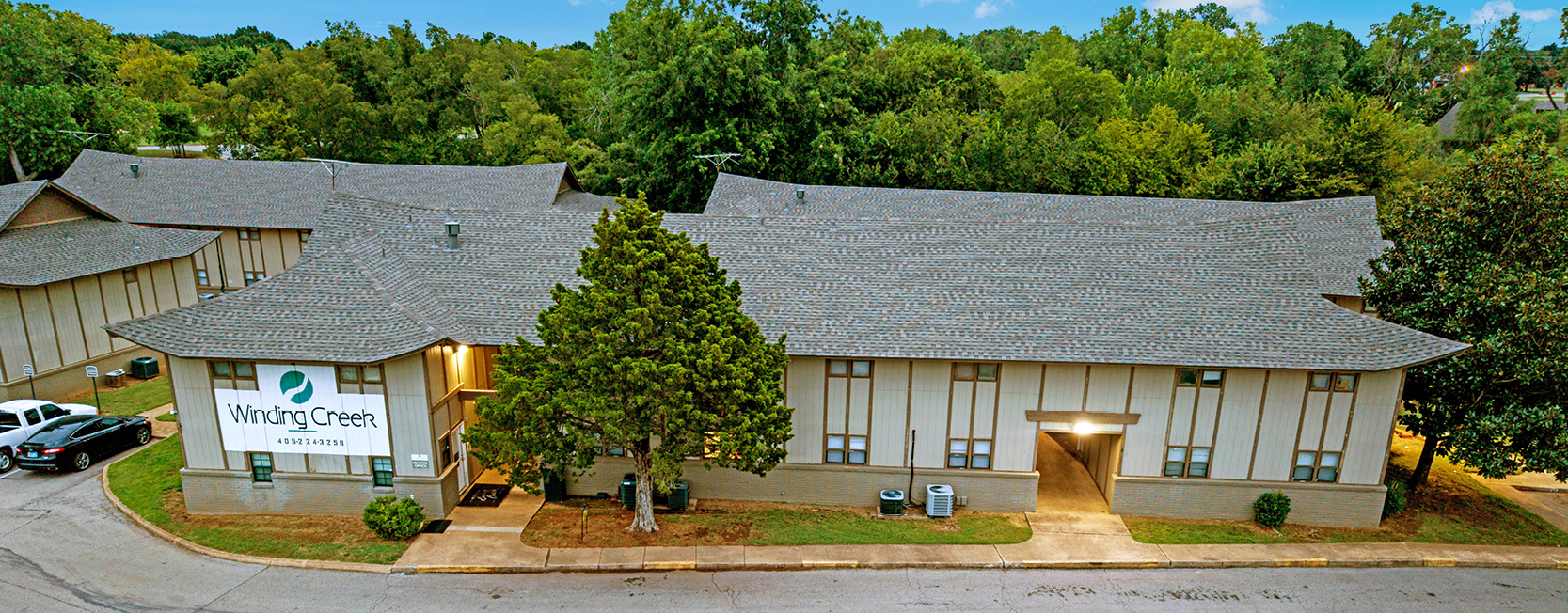 Aerial view of Winding Creek Apartments featuring unique, curved rooflines and a large sign on the building exterior, surrounded by mature trees and a quiet residential street.